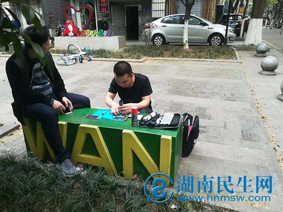 工程師在街邊石板凳為顧客維修手機。